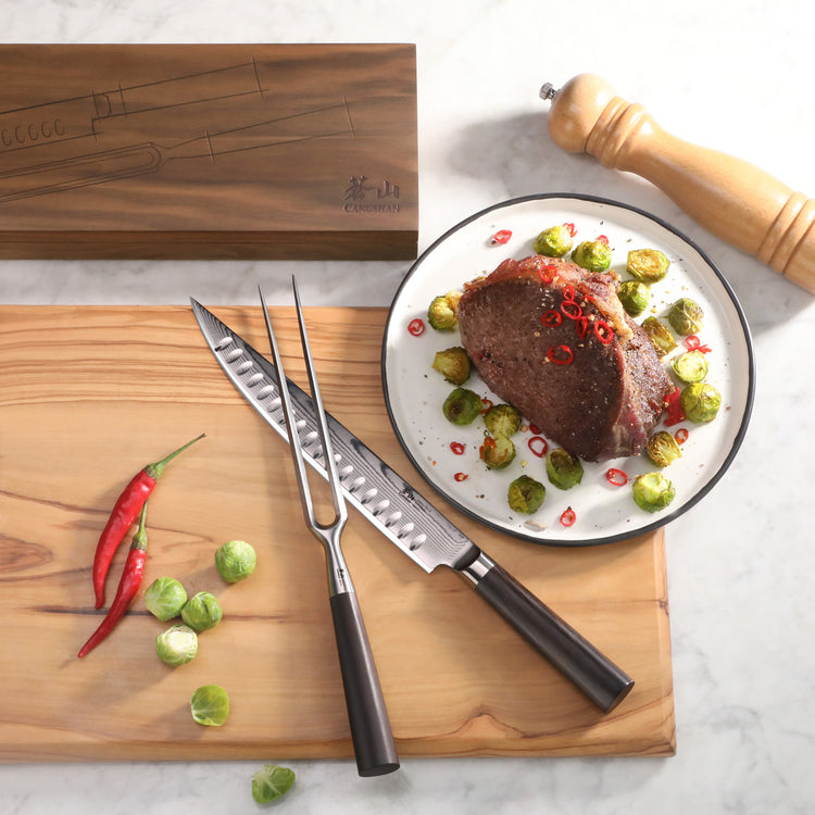 Two-piece carving set with black handles on a wooden board next to a plate of cooked meat garnished with Brussels sprouts and