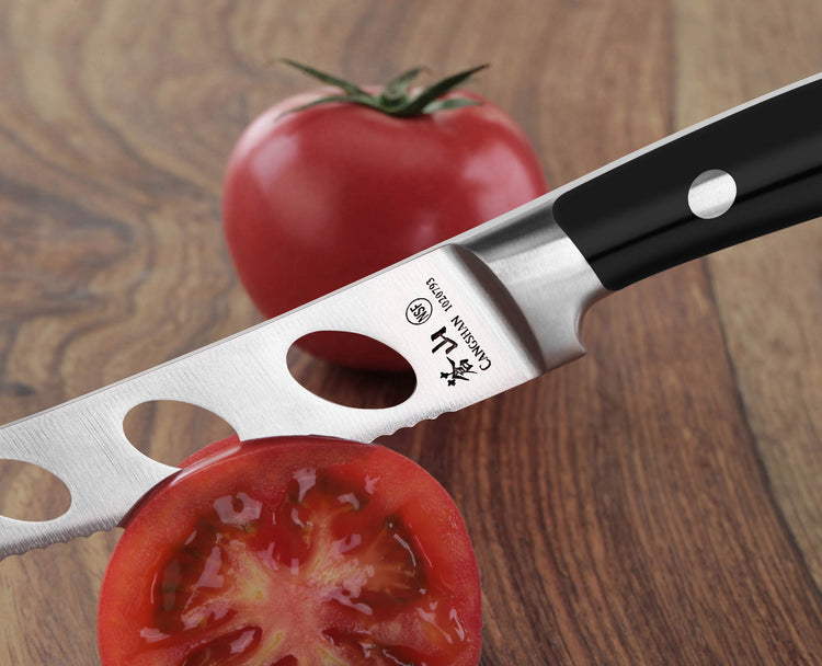 Tomato knife with black handle and holes in blade cutting a sliced tomato on a wooden surface with whole tomato in background
