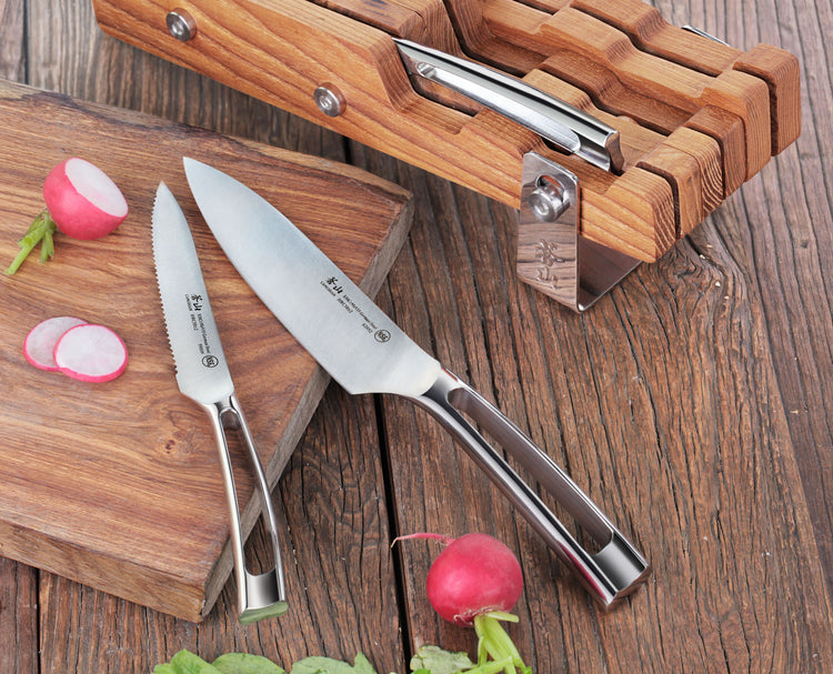 Two stainless steel knives with wooden handles on a cutting board next to sliced radishes and a wooden knife block.