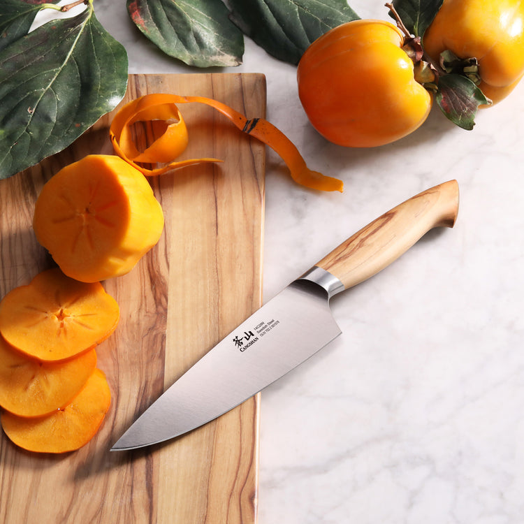 6-inch chef's knife with wooden handle on a cutting board next to sliced and peeled persimmons.