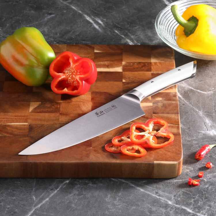 8-inch chef's knife on wooden cutting board with sliced red bell pepper and whole green and yellow peppers nearby