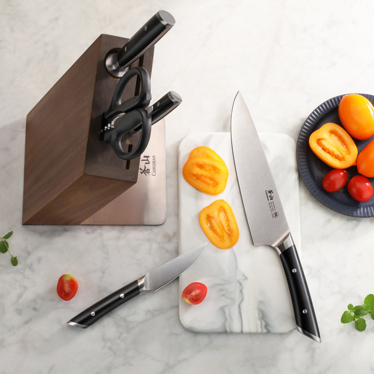 Six-piece knife set with two knives, kitchen scissors in a wooden block, and sliced yellow bell peppers on a marble surface.