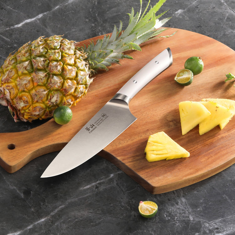8-inch chef's knife on wooden cutting board with whole pineapple, lime, and pineapple slices.