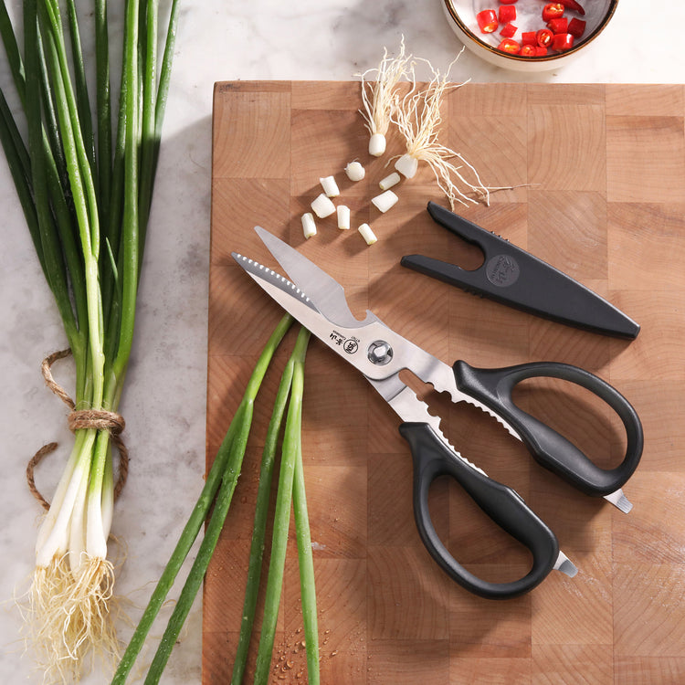 Black-handled kitchen shears with serrated blades and a black blade holder on a wooden cutting board with chopped green onion