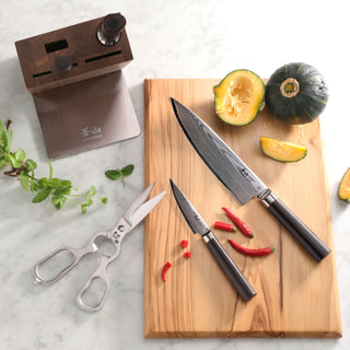 
                    
                      Two Damascus steel knives with dark handles on a wooden cutting board next to a halved green squash and red chili peppers, wi
                    
                  
