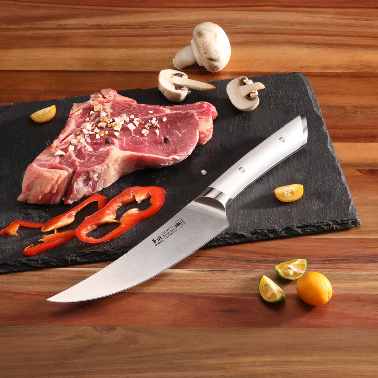 Boning knife with stainless steel blade and handle on a cutting board with raw steak, mushrooms, red pepper, and small citrus