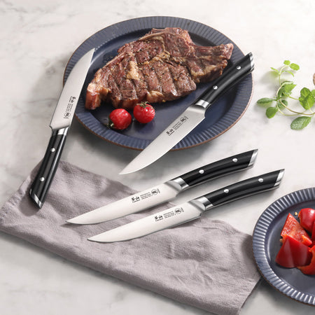 Four steak knives with black handles and stainless steel blades, one cutting a grilled steak on a blue plate with cherry toma
