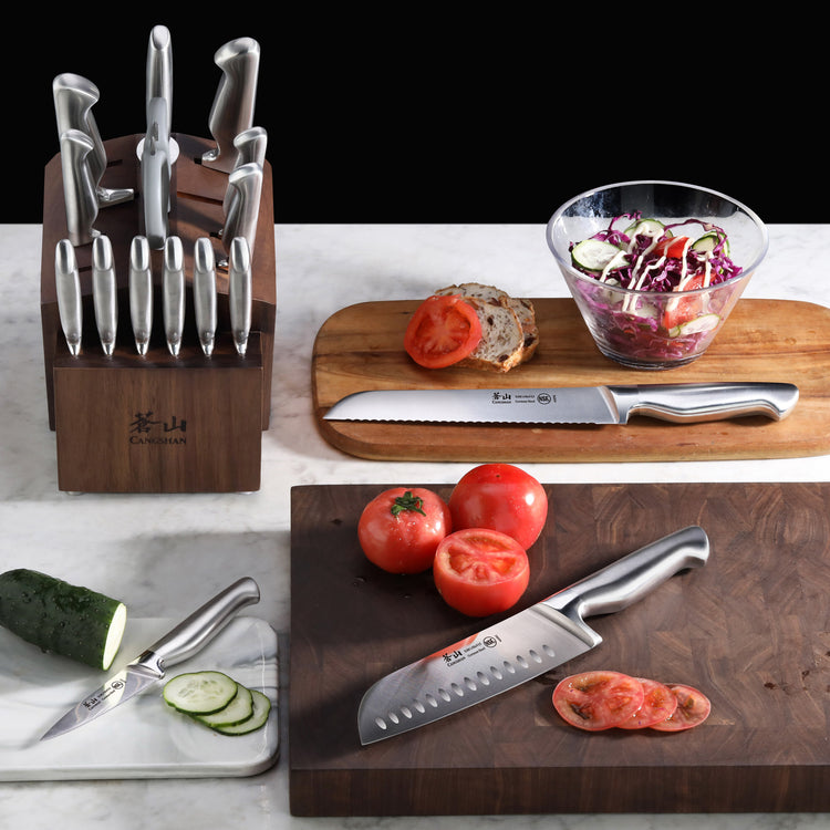17-piece knife set in acacia block with stainless steel knives, displayed with sliced tomatoes, cucumber, bread, and salad.