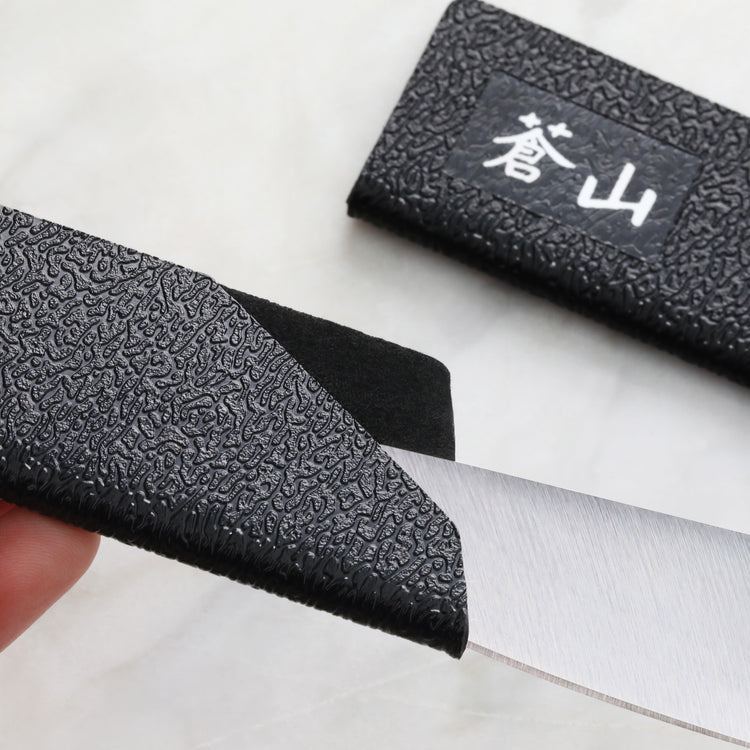 Black textured knife guard partially covering a steak knife blade, with a matching sheath nearby.