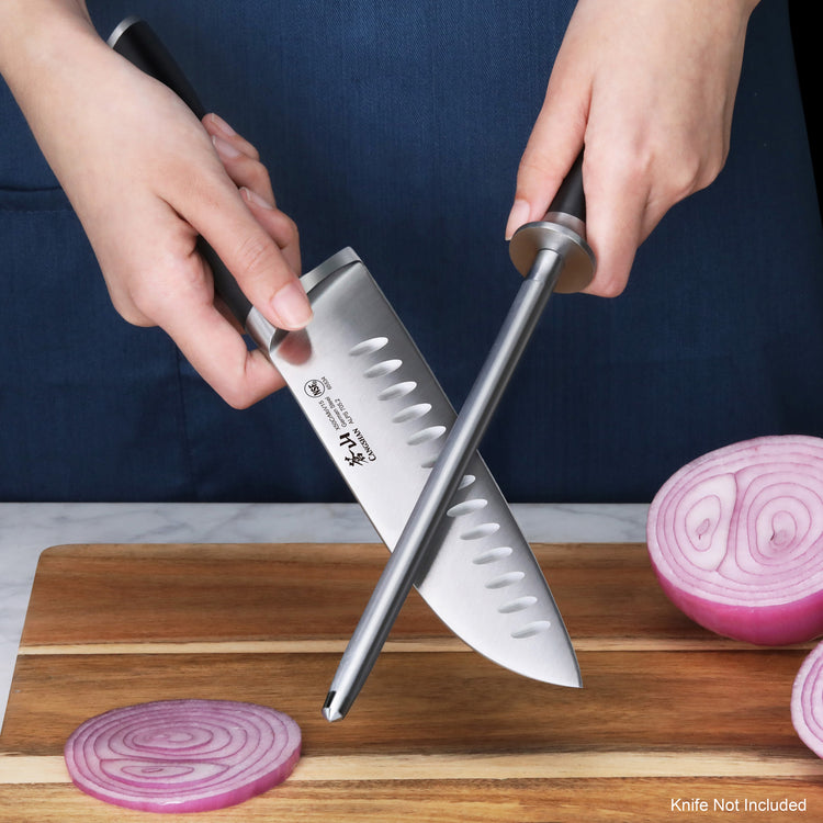 Hands holding a honing steel and a knife blade positioned for sharpening on a wooden cutting board with sliced red onions nea