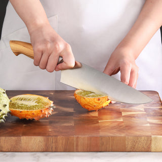 
                    
                      Person using an 8-inch chef's knife with an olivewood handle to cut a kiwano fruit on a wooden cutting board.
                    
                  