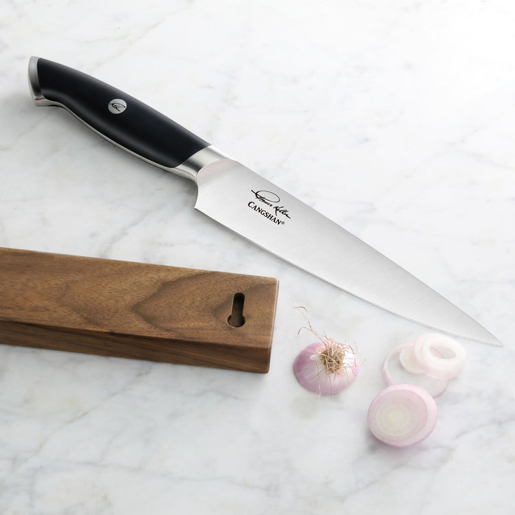 Chef's knife with black handle and engraved signature, wooden magnetic knife block, whole and sliced shallot on marble surfac