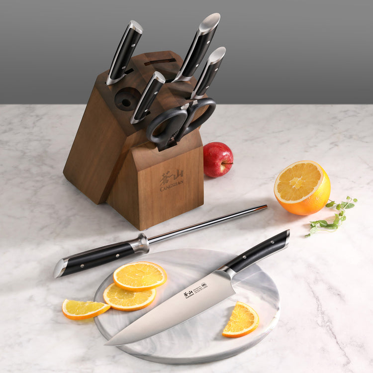 Wooden knife block holding six knives and a pair of scissors, with a chef's knife and sharpening steel on a marble surface ne