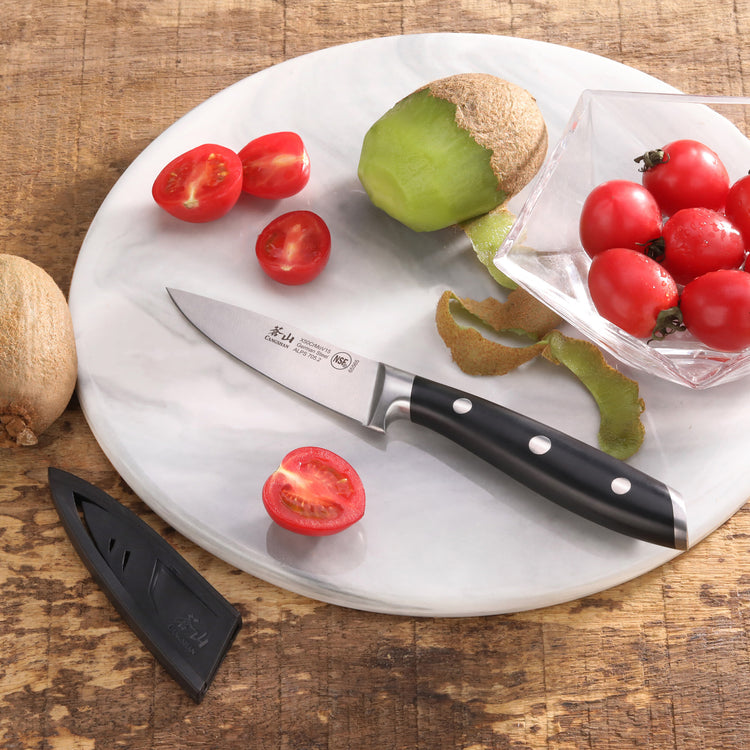 Paring knife with black handle on a round white cutting board with halved cherry tomatoes and peeled kiwi fruit.