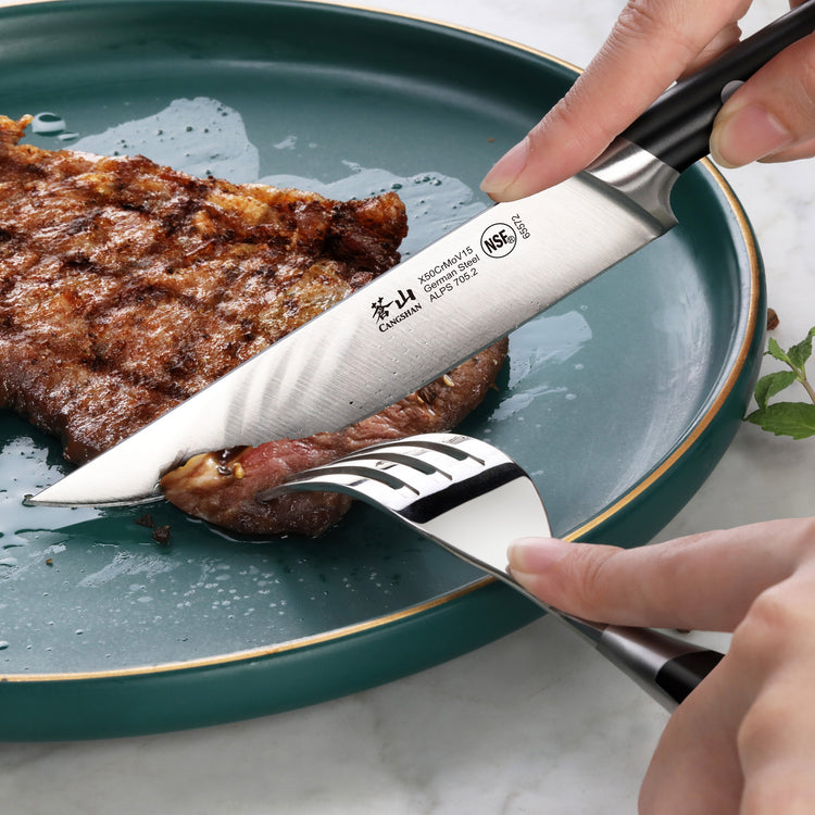 Hand using a black-handled steak knife to cut a cooked steak on a green plate, held by a fork.