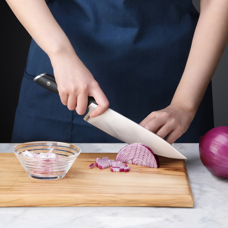 Person slicing a red onion on a wooden cutting board using a black-handled chef's knife.