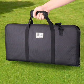 
                    
                      Black rectangular carrying bag with handles held by a hand, placed on green grass.
                    
                  