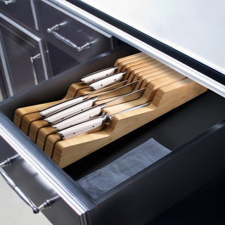 
                    
                      Seven stainless steel knives with white handles arranged in a bamboo in-drawer knife organizer inside a kitchen drawer.
                    
                  