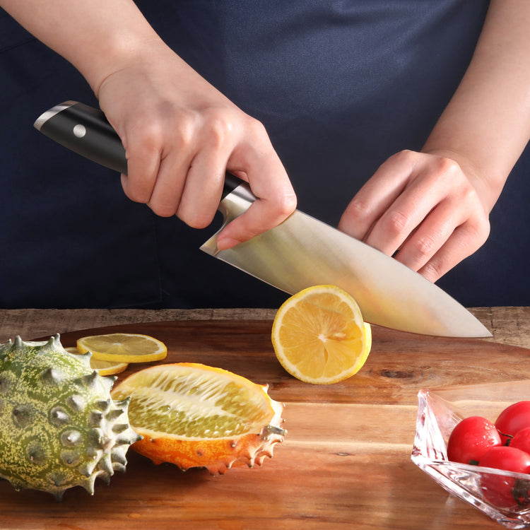 Person slicing a yellow fruit on a wooden cutting board with a black-handled chef's knife.