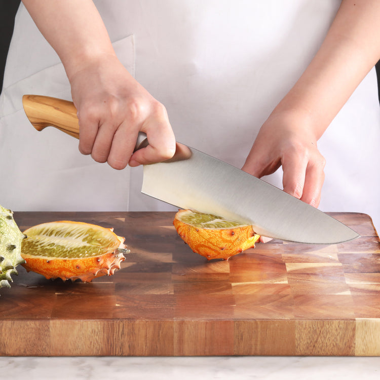 Person slicing a horned melon on a wooden cutting board with a large kitchen knife.