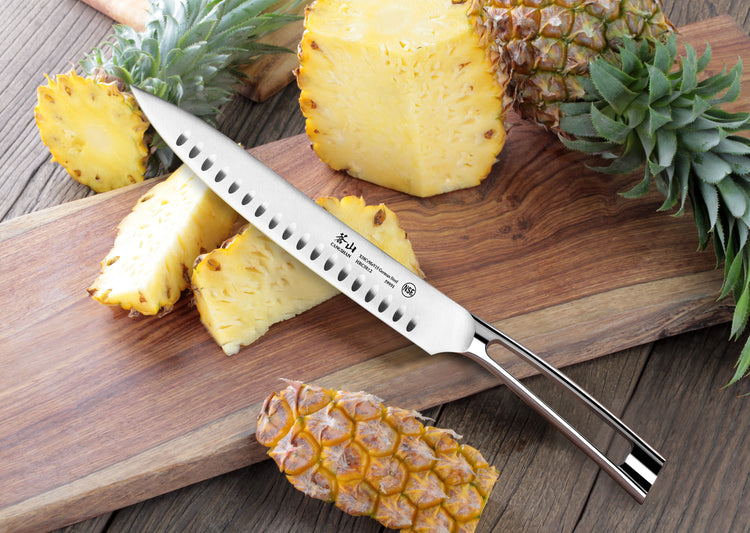9-inch carving knife with hollow edge on wooden board next to sliced and whole pineapples.