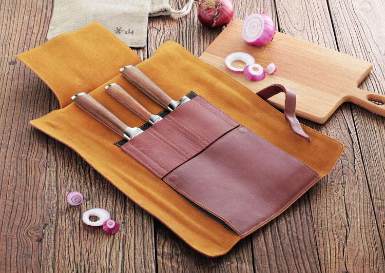 Four knives with wooden handles in a brown leather roll-up case on a wooden surface, next to sliced red onions and a cutting