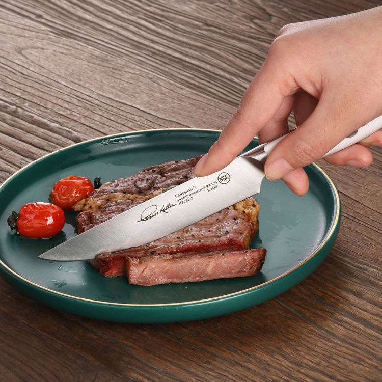 Hand holding a steak knife cutting a cooked steak on a green plate with two roasted cherry tomatoes.
