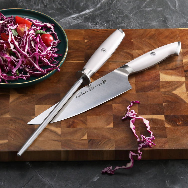 White-handled honing steel and chef's knife on wooden cutting board with shredded red cabbage and salad bowl.